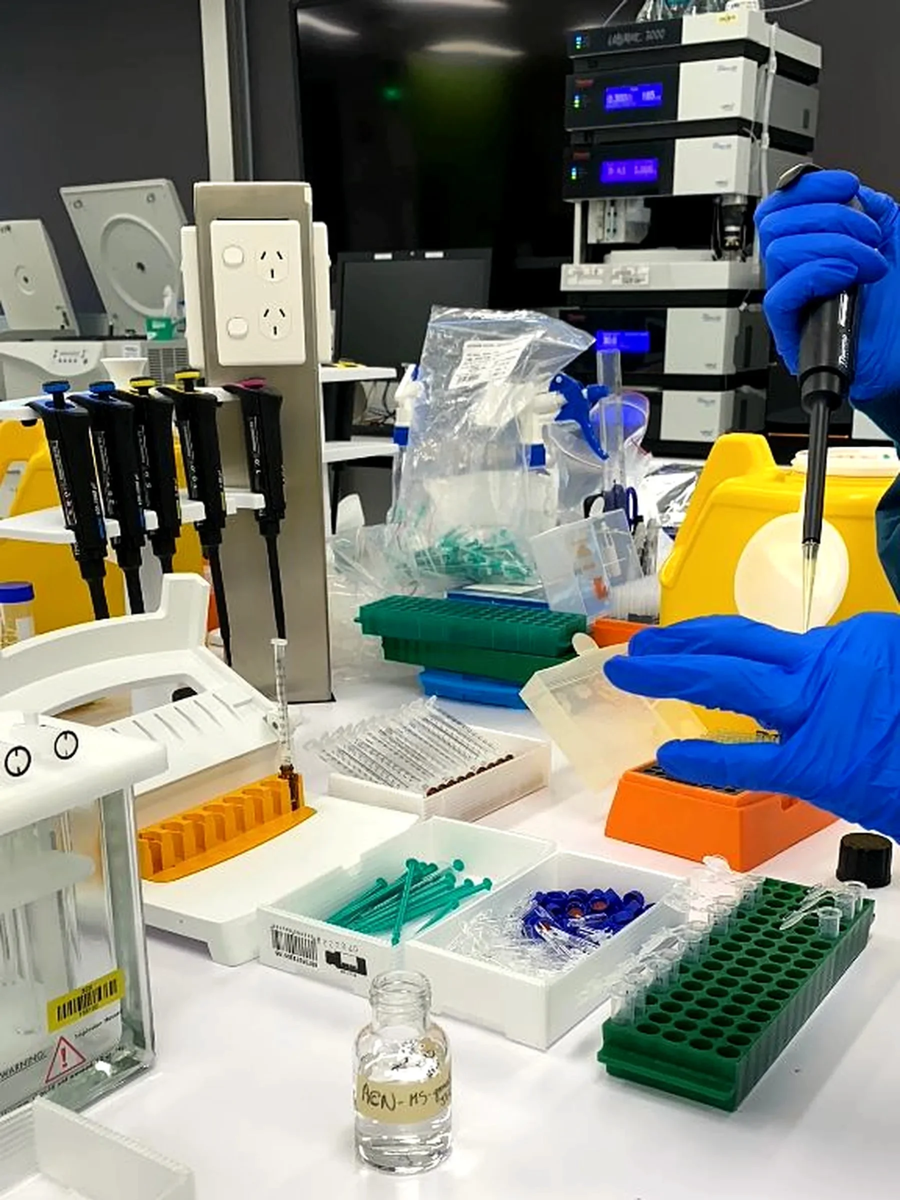 Gloved hands pipetting samples in a working analytical chemistry lab.